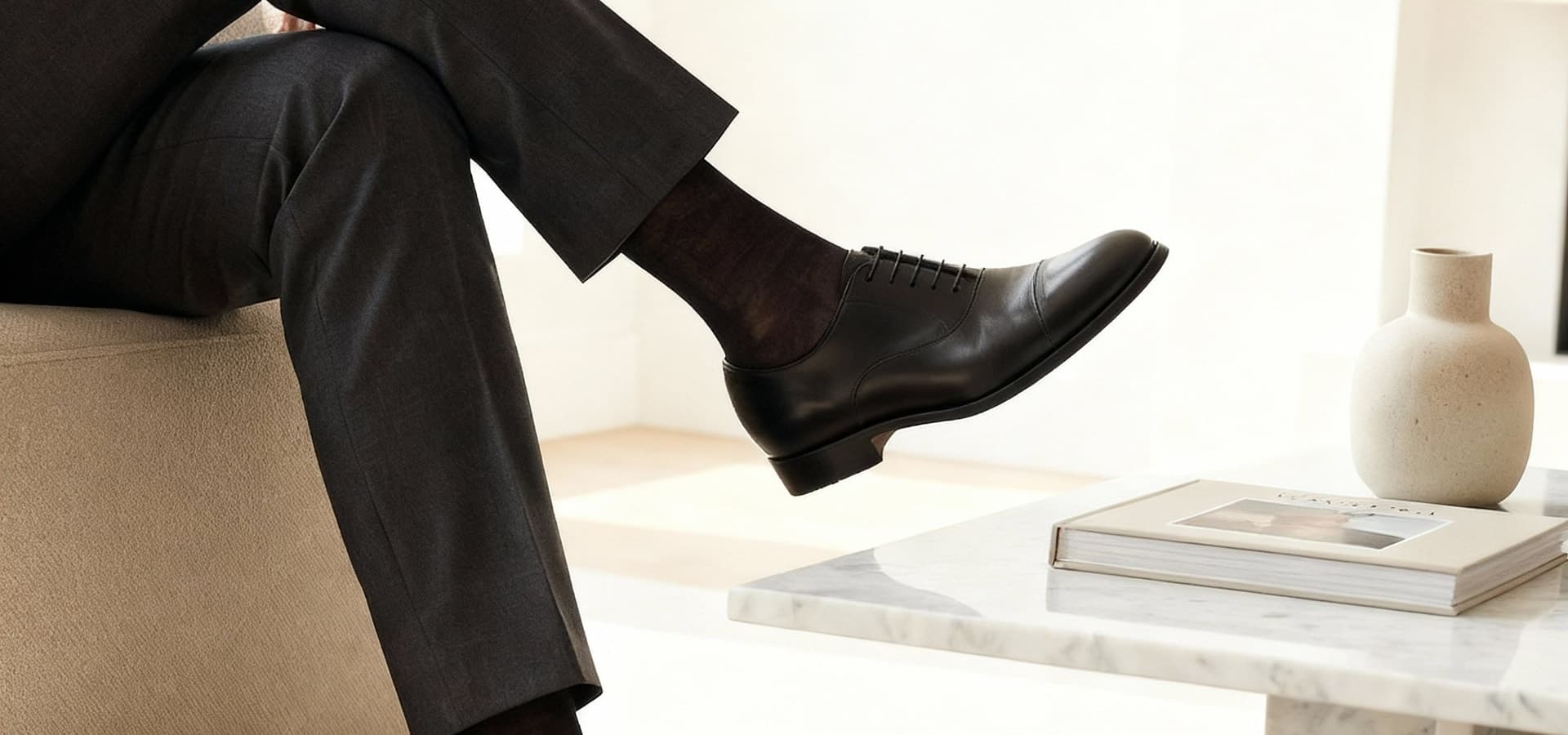 Hombre elegante sentado con calcetines finos y zapatos Oxford negros sobre mobiliario minimalista