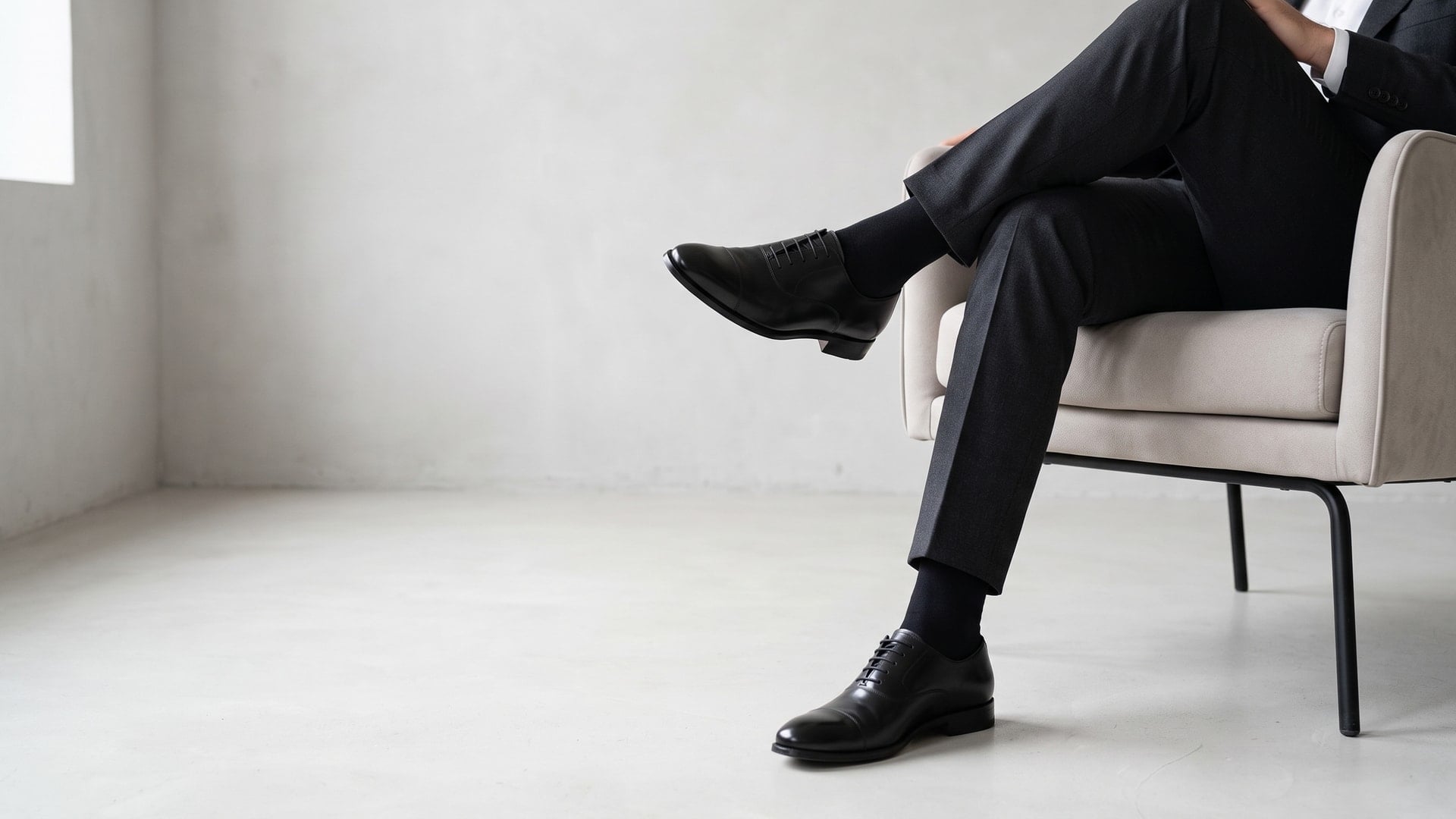 Mann im dunklen Anzug sitzend mit langen schwarzen Baumwollsocken unter der Hose